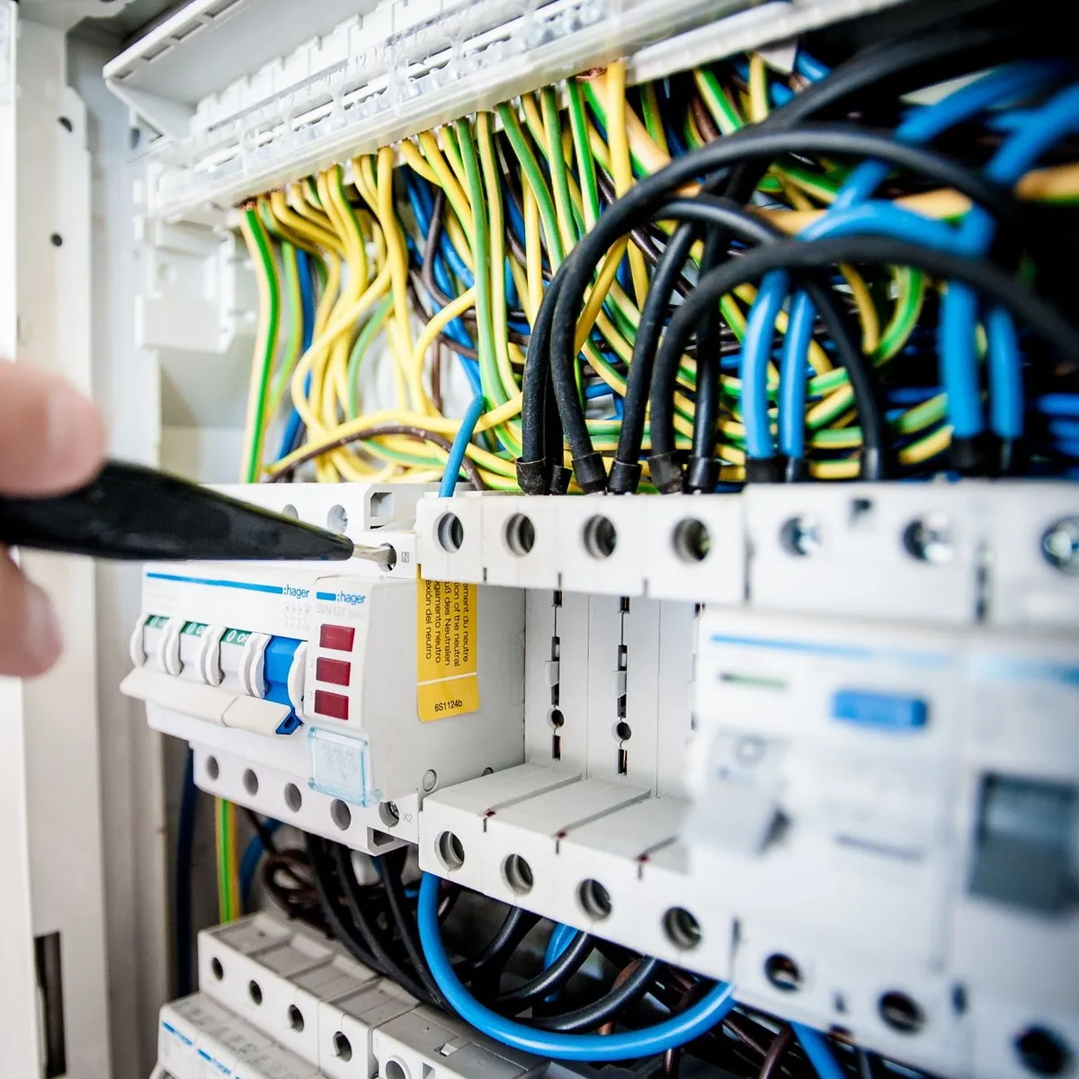 Circuit breakers in an open consumer unit being checked with a voltage tester
