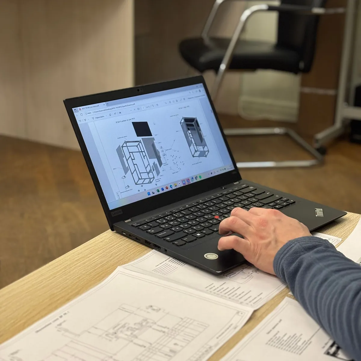 Electrical engineer reviewing a layout drawing on a laptop beside printed design drawings
